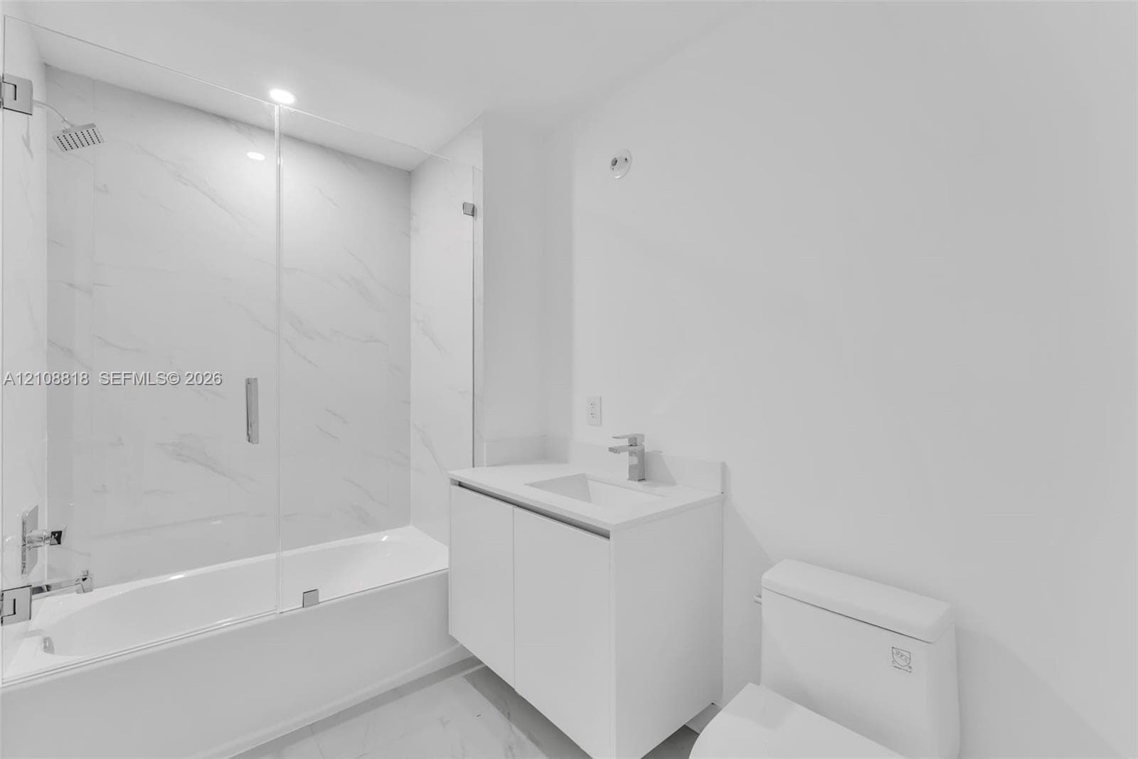 Bathroom featuring a vanity with an integrated basin, a soaking tub with a frameless glass enclosure, and wall-surround tile with veined patterning