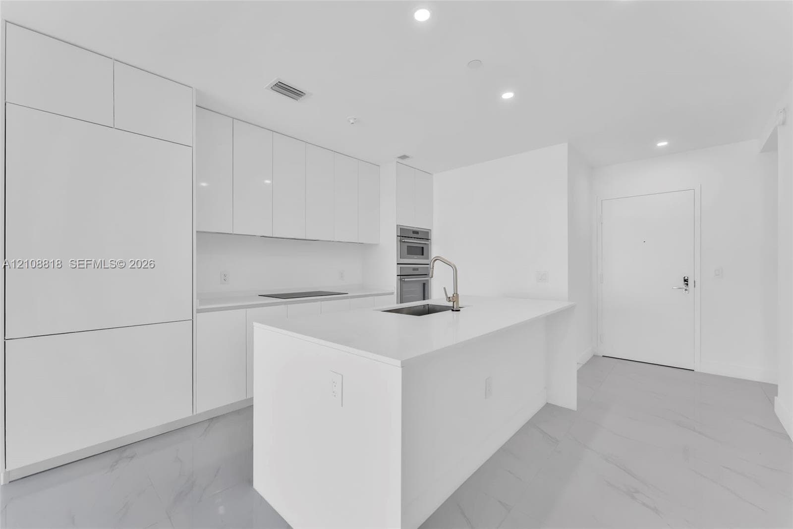 Contemporary kitchen featuring white flat-panel cabinetry, a central island with a solid-surface countertop, an undermount sink with a gooseneck faucet, built-in stainless steel appliances, and large-format flooring