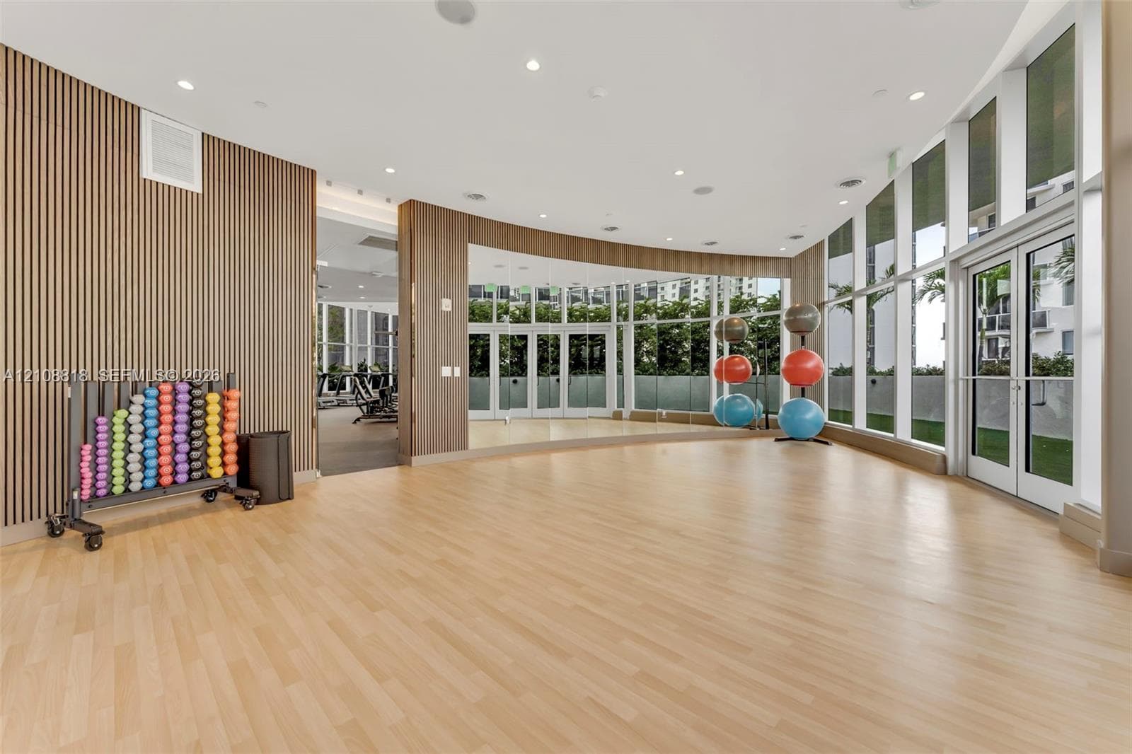 Fitness studio featuring wood-finish flooring, full-length wall mirrors, floor-to-ceiling windows, and decorative slat wood wall paneling