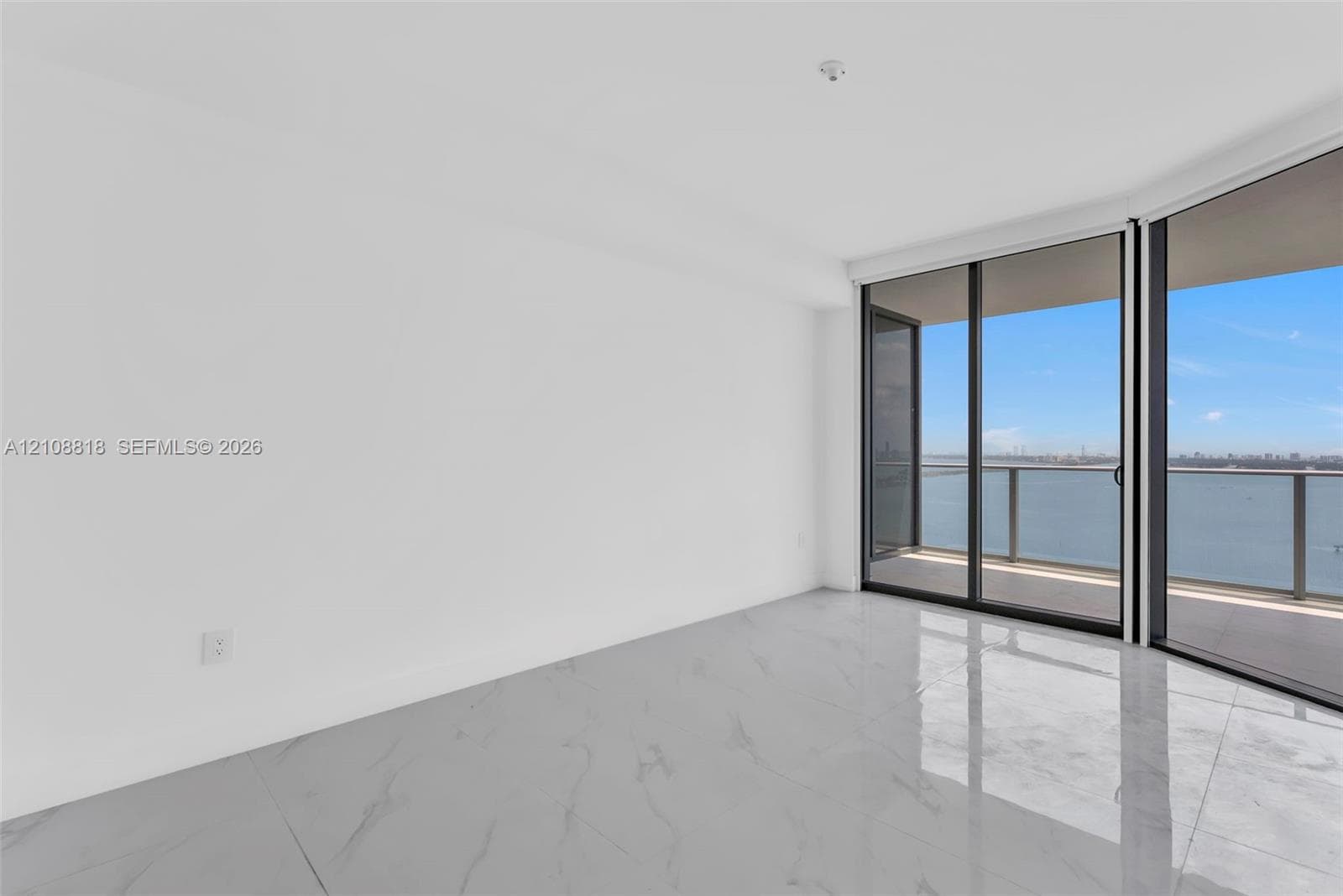 Expansive room featuring large-format tile flooring, floor-to-ceiling glass sliding doors, and a covered balcony with a water backdrop