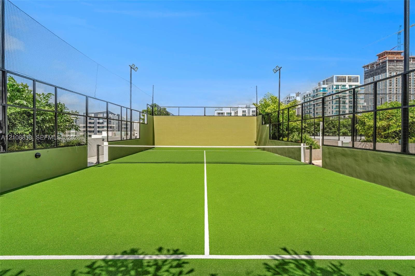 Paddle court featuring a synthetic turf surface, high-perimeter black metal fencing, integrated floodlighting, and solid concrete walls