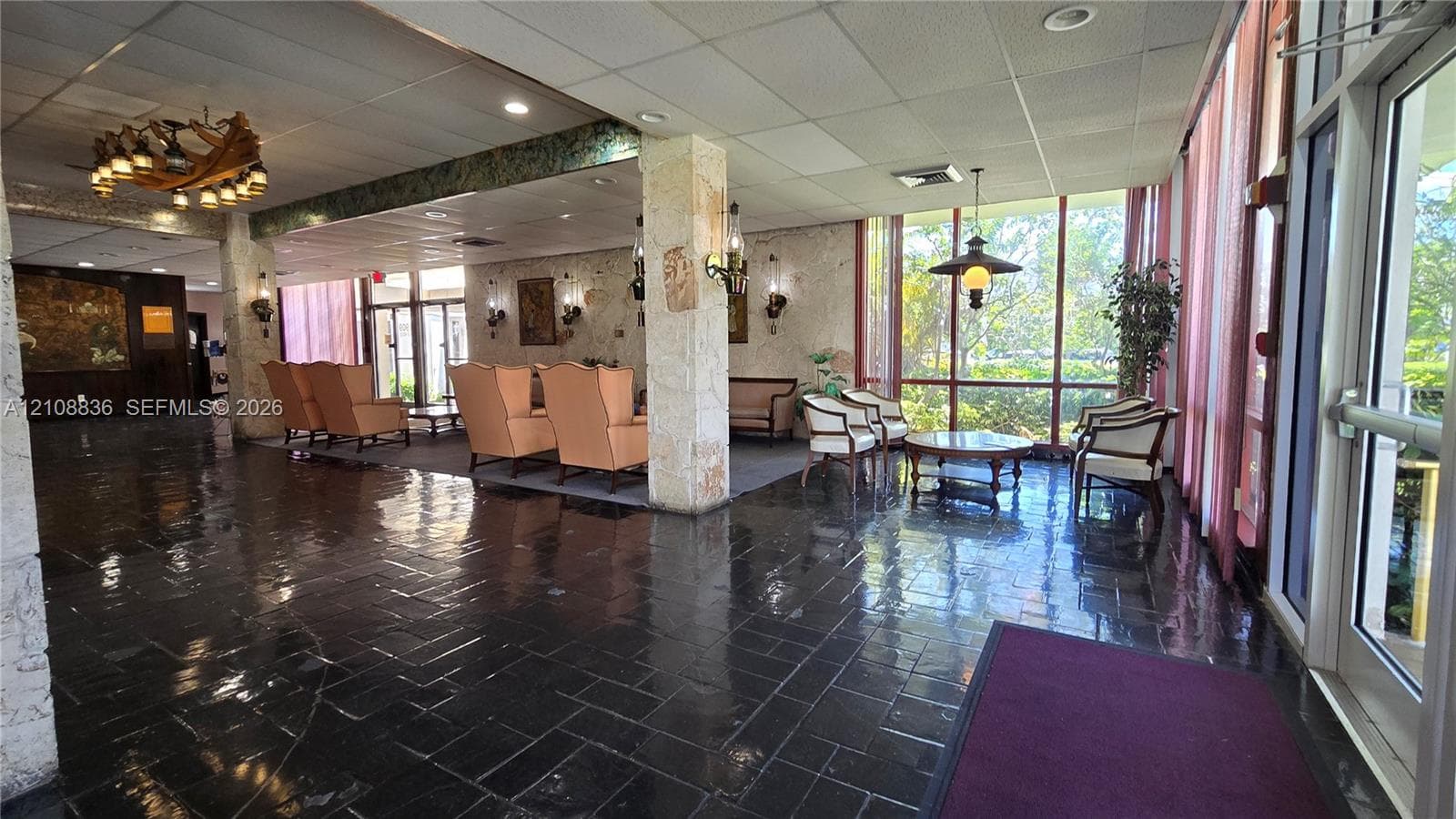 Spacious lobby featuring stone-clad structural pillars, dark stone tile flooring, floor-to-ceiling windows, and decorative chandelier lighting