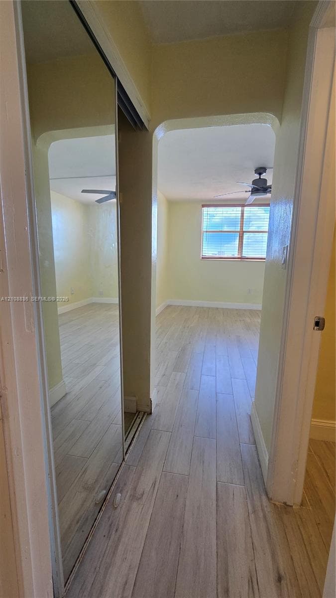 Full-height mirrored sliding closet doors featuring wood-finish flooring, arched doorway detail, and a ceiling-mounted fan fixture