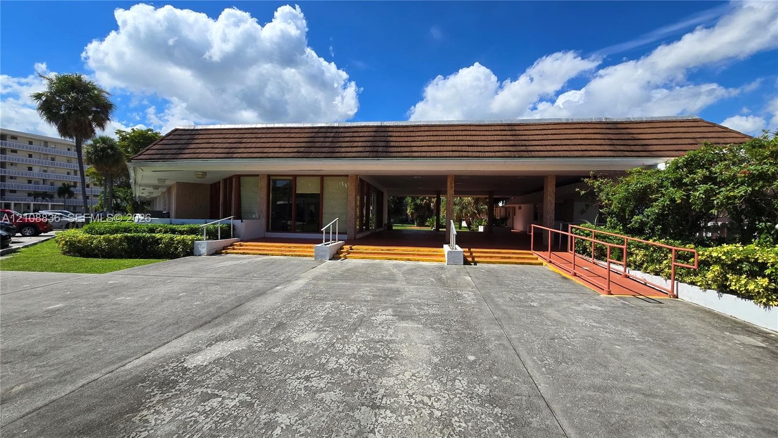 Exterior facade featuring a wide covered entryway, terra-cotta style tiled steps, structural support columns, and an integrated metal access ramp