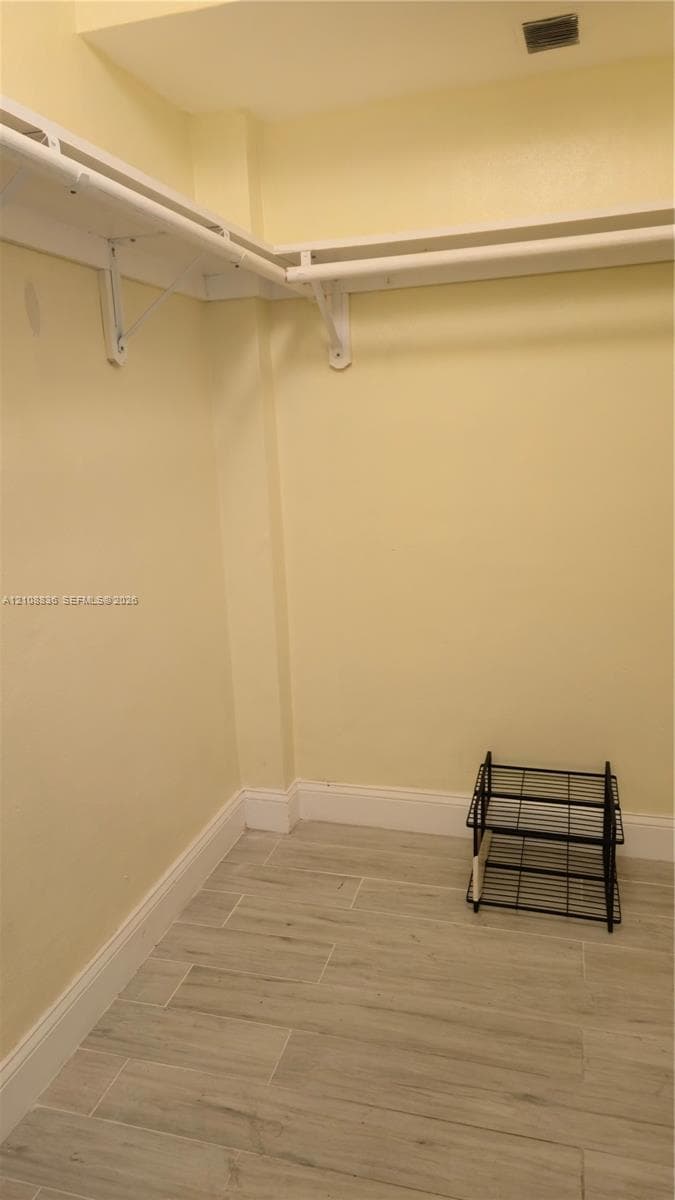 Walk-in storage area featuring wood-finish tile flooring and wraparound white shelving