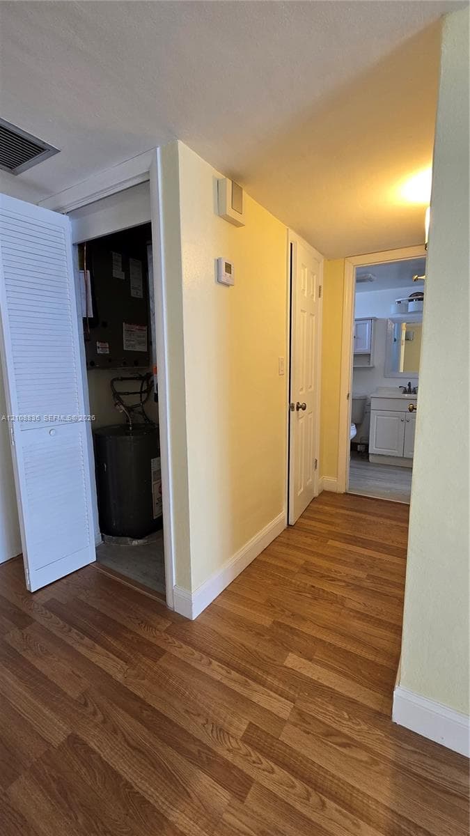 Hallway featuring wood-finish flooring, louvered closet doors, and a utility closet containing a water heater and HVAC unit
