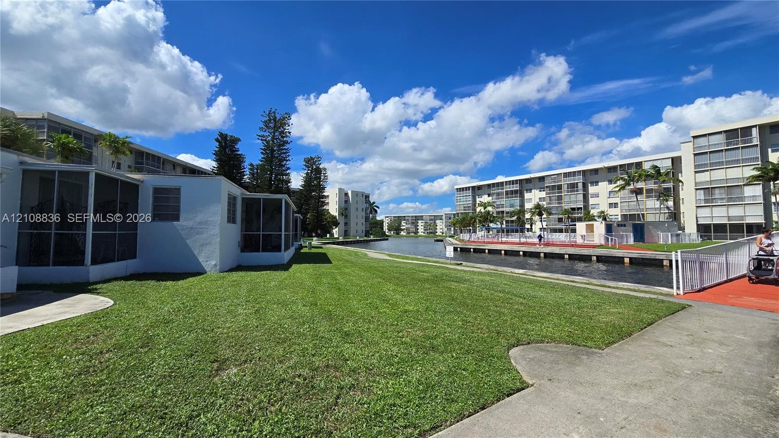 Ground-level exterior featuring screen-enclosed patios, expansive turf lawn, concrete walkways, and canal frontage