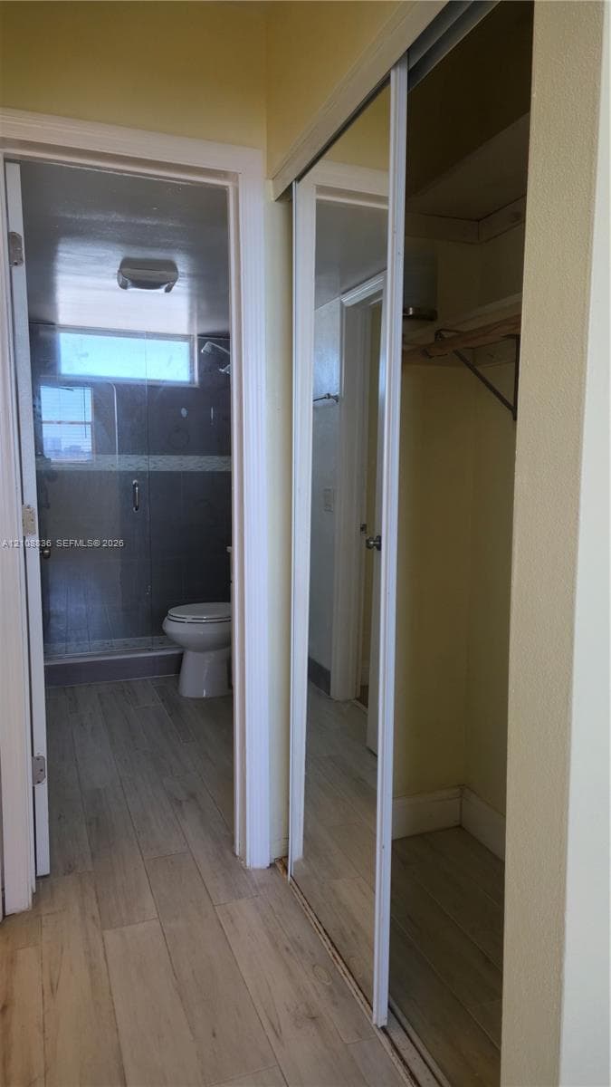 Sliding mirrored closet doors, wood-finish flooring, and a walk-in shower with a glass enclosure