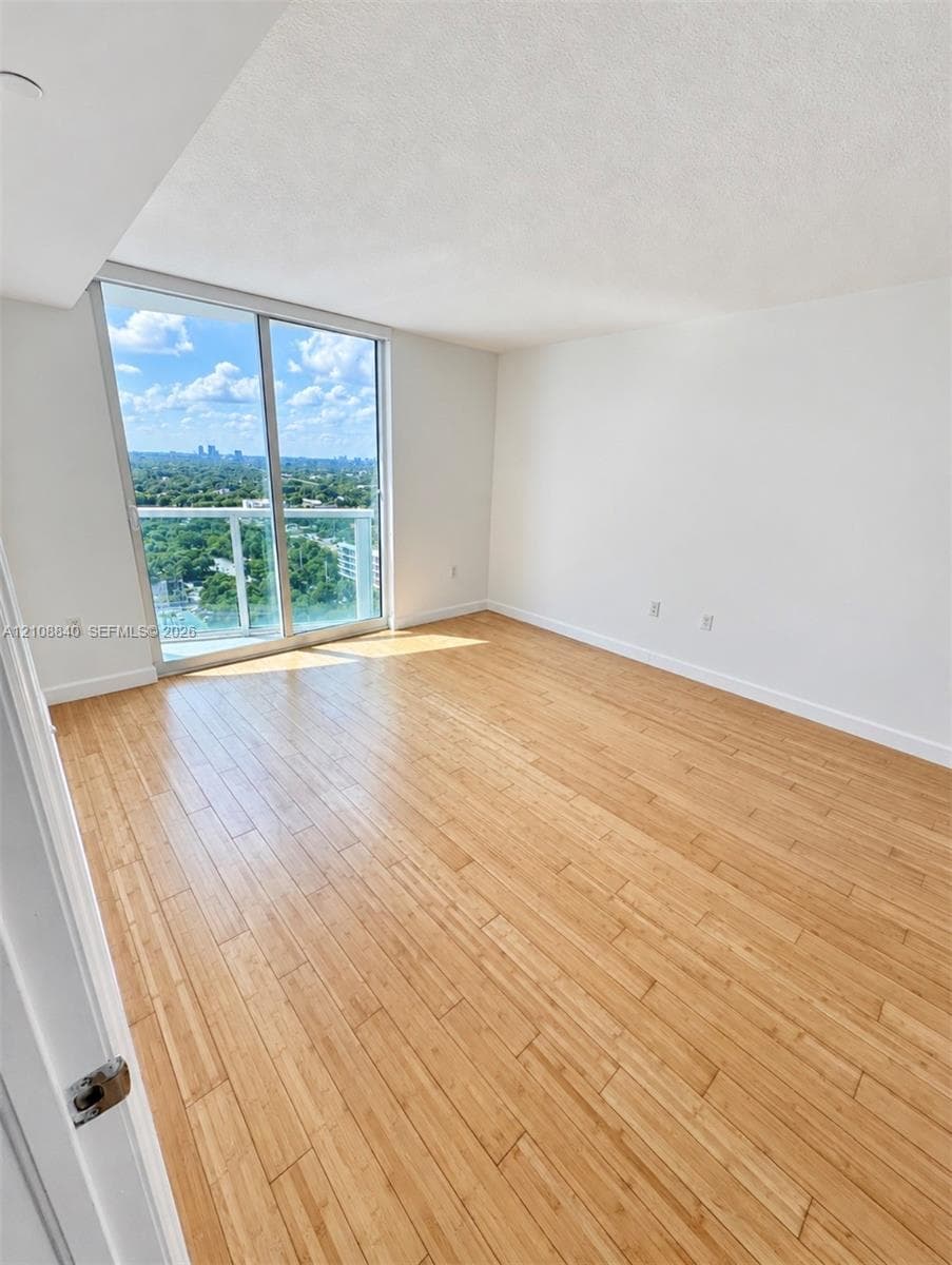 Wood-finish flooring, full-height windows, and sliding glass door leading to a balcony with glass railing