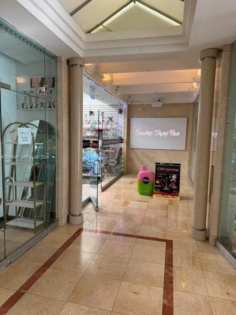 Commercial storefront featuring polished stone flooring with decorative inlay, glass-paneled entry, structural stone columns, and recessed tray ceiling with skylight