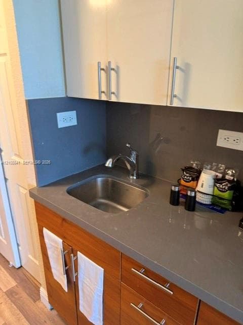 Wet bar featuring wood-finish cabinetry, gray solid-surface countertop, integrated stainless steel sink, polished chrome faucet, and matte-finish gray backsplash