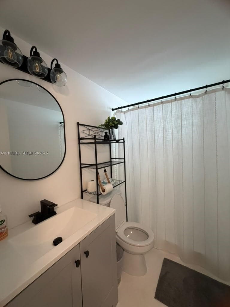 Gray vanity featuring a solid surface countertop with an integrated rectangular basin, matte black faucet, circular wall-mounted mirror, and three-globe light fixture