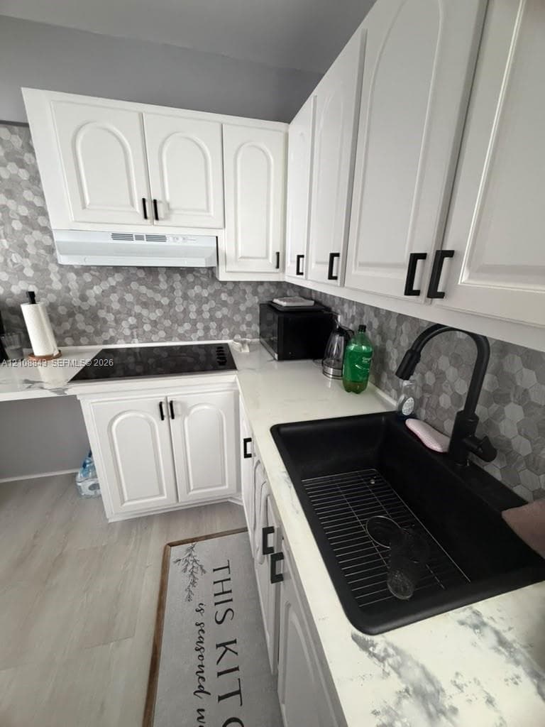 Kitchen featuring white cabinetry with matte black hardware, stone-finish countertops, geometric tile backsplash, undermount sink with a gooseneck faucet, and an integrated electric cooktop