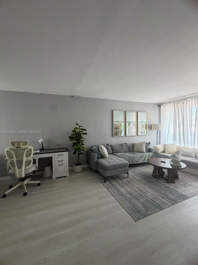 Open-concept interior featuring neutral wall paint, wood-finish flooring, and large-scale windows with floor-to-ceiling drapery