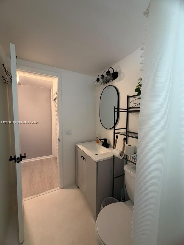 Bathroom featuring a grey shaker-style vanity with a solid surface countertop, matte black faucet, oval wall mirror, and matching three-light vanity fixture