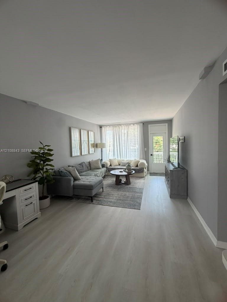 Open-concept interior featuring neutral wall tones, light wood-finish flooring, and a glass-paneled exterior door