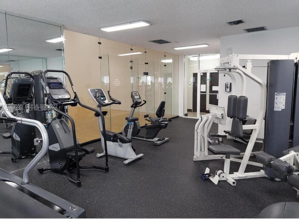 Fitness center featuring rubber flooring, floor-to-ceiling mirrors, and an enclosed racquetball court with glass paneling