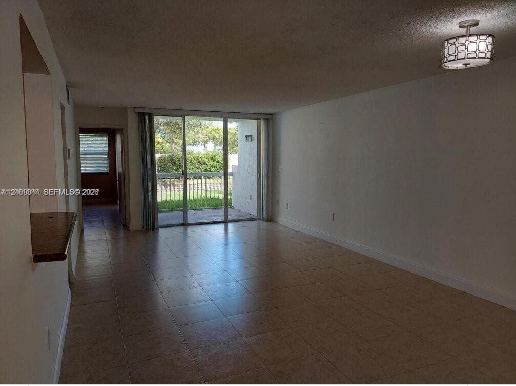 Living area featuring tile flooring, a pass-through opening, a drum-style ceiling fixture, and sliding glass doors with access to an exterior terrace