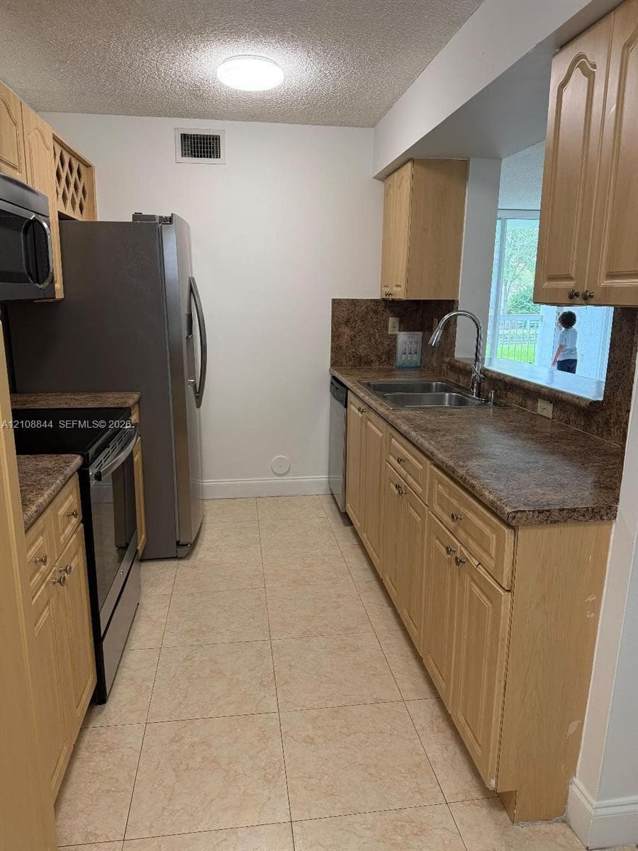 Kitchen featuring light-finish cabinetry, stone-texture countertops, stainless steel appliances, ceramic tile flooring, and a window pass-through