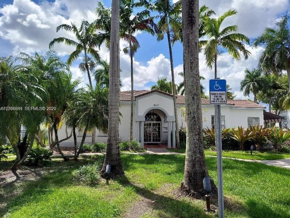 Stucco exterior featuring an arched entryway, terracotta-style roof tiles, and mature palm landscaping