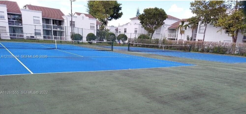 Multi-court recreational facility featuring two tennis courts with high-perimeter chain-link fencing and mature perimeter landscaping