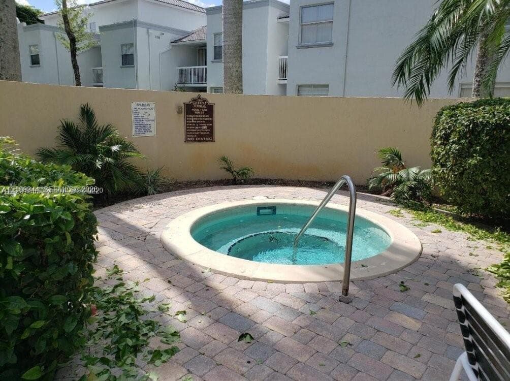 In-ground circular spa featuring a concrete surround, paver decking, integrated metal handrail, and perimeter privacy wall