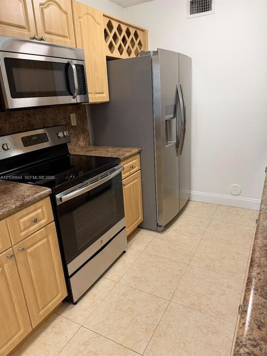 Kitchen featuring light wood cabinetry, integrated wine storage, stainless steel appliance suite, patterned laminate countertops, and tile flooring