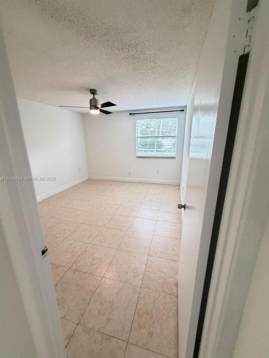 Room featuring neutral tile flooring, light-toned wall finishes, a ceiling-mounted light fixture with fan, and a single-pane window
