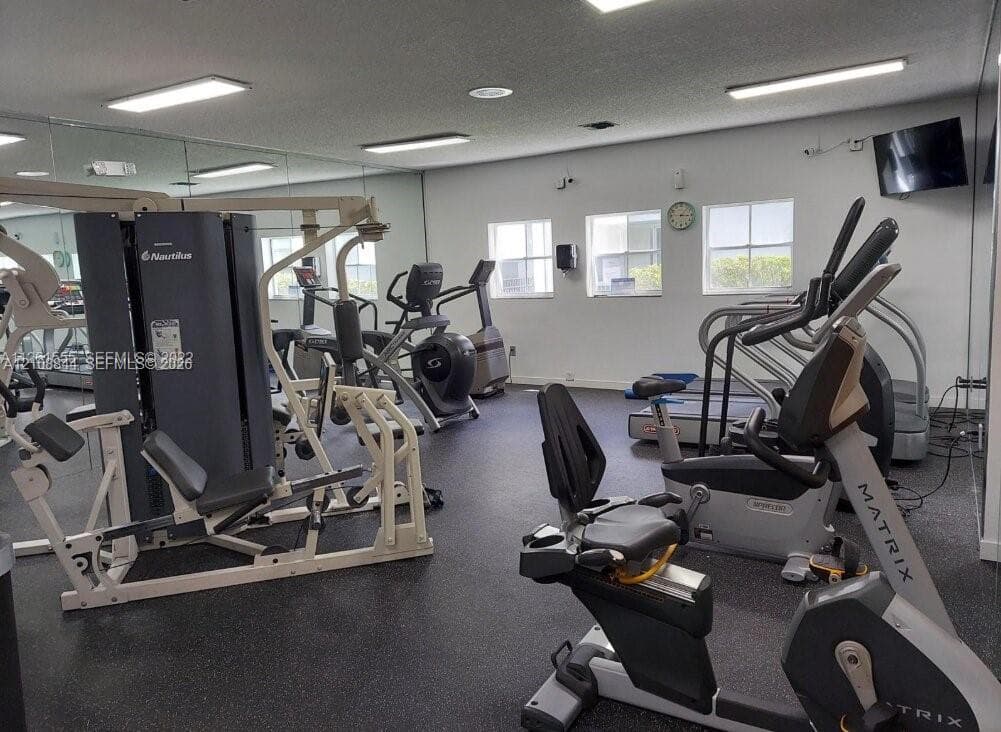 Fitness center featuring rubberized flooring, expansive wall-to-wall mirrors, recessed overhead lighting, and multi-pane windows