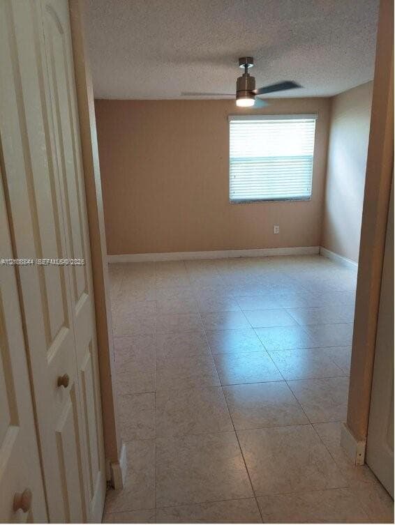 Room featuring neutral tile flooring, multi-panel bi-fold closet doors, a brushed-nickel ceiling fan, and horizontal window blinds