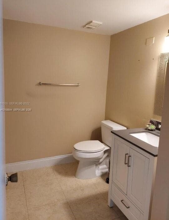 White vanity featuring a solid surface countertop with an integrated basin, ceramic toilet, wall-mounted towel bar, and large-format tile flooring