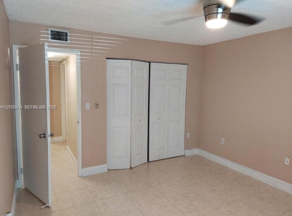 Room featuring tile flooring, neutral wall paint, multi-panel bifold closet doors, and a ceiling fan with integrated lighting