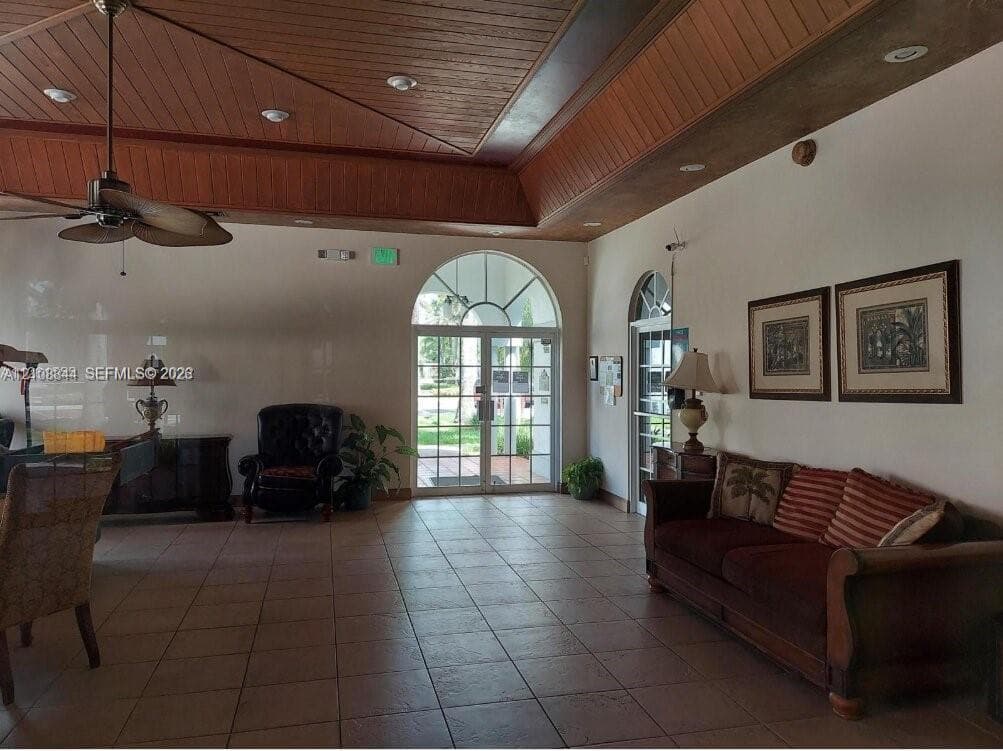 Vaulted tray ceiling with wood plank paneling, tile flooring, and arched glass entryway