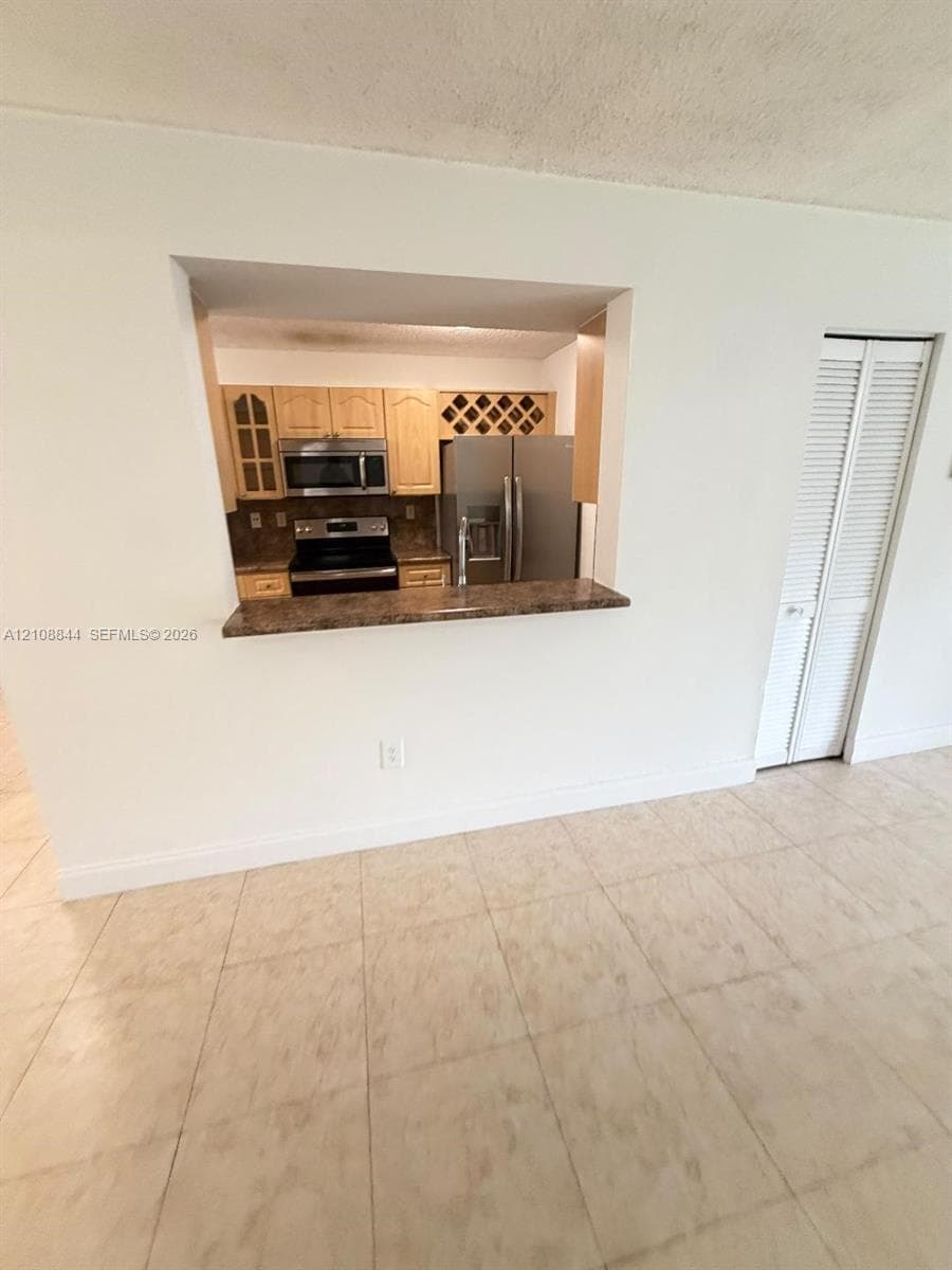 Kitchen pass-through window featuring a stone-finish countertop, light wood cabinetry, integrated wine storage, stainless steel appliances, and tile flooring