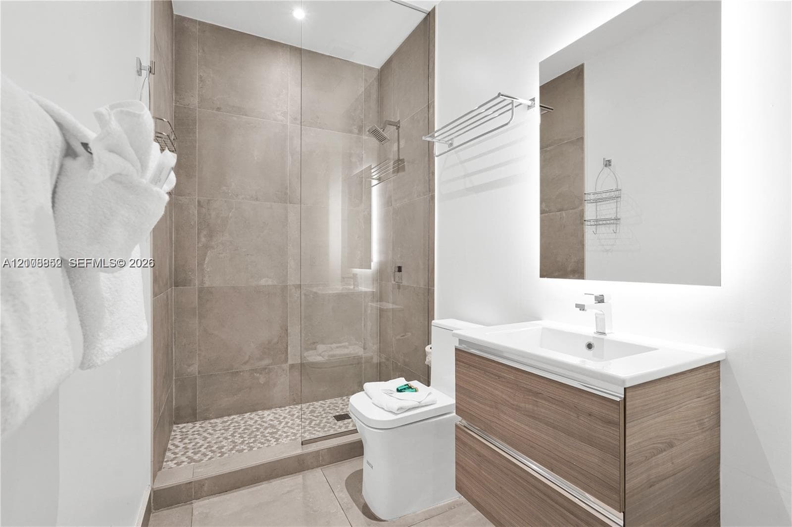 Modern bathroom featuring a wood-finish dual-drawer vanity, a rectangular sink with a chrome faucet, a frameless glass-enclosed shower with large-format stone-tile walls, and pebble-textured shower floor tile