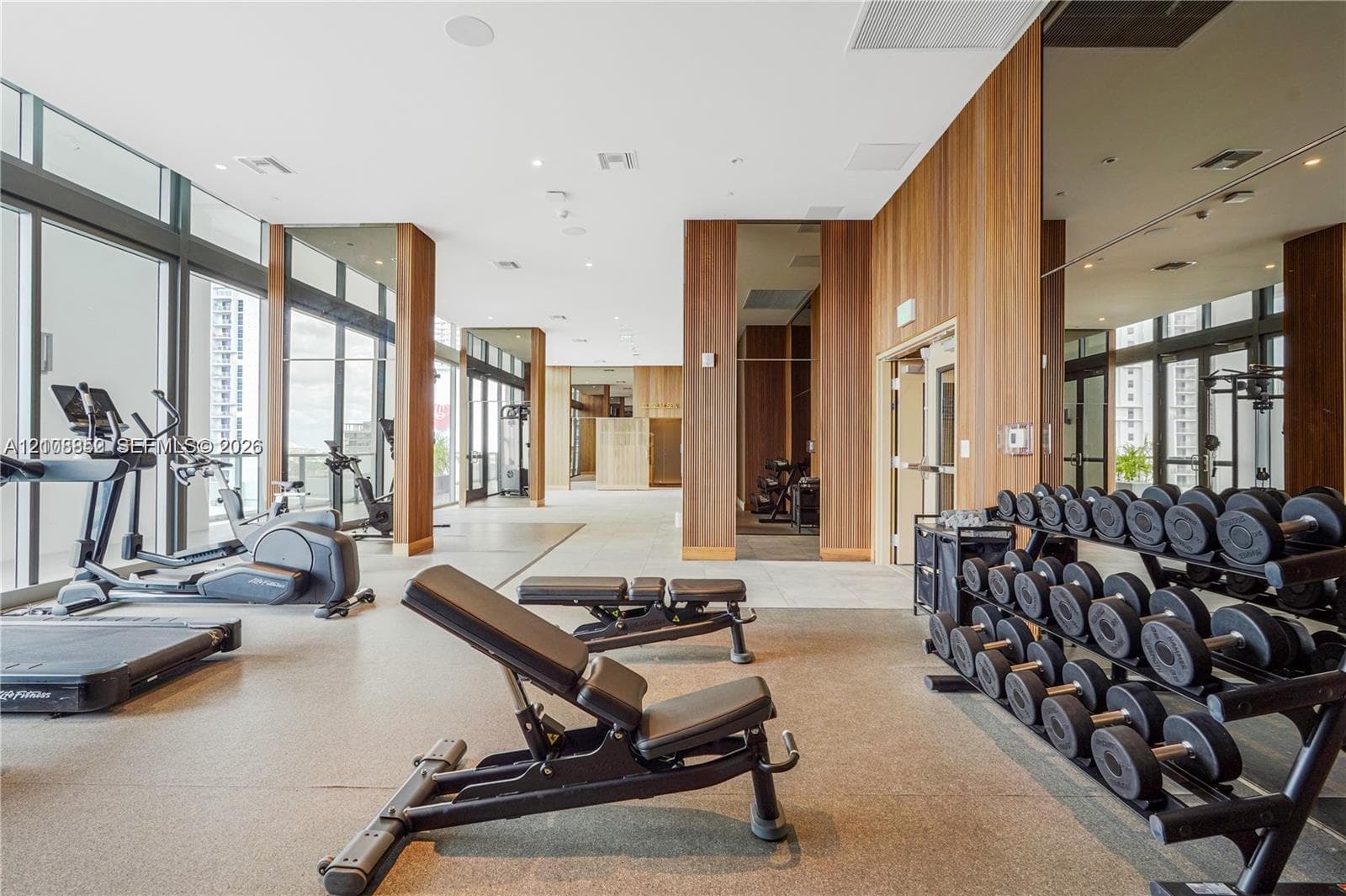 Fitness center featuring floor-to-ceiling windows, wood-paneled walls, mirrored accents, recessed ceiling lighting, and resilient flooring