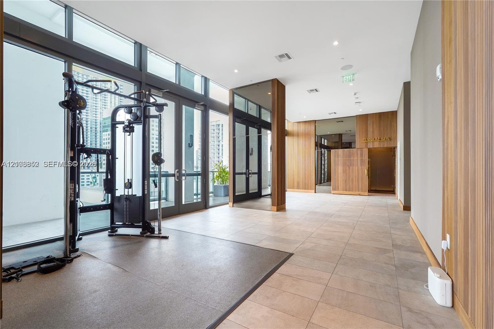 Fitness space featuring floor-to-ceiling windows, wood-paneled walls, recessed ceiling lighting, and large-format tile flooring