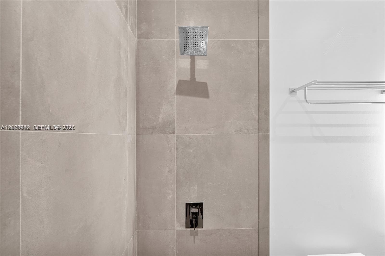 Shower featuring large-format neutral-toned wall tile, a square rainfall showerhead, a built-in single-handle shower valve, and a wall-mounted metal towel rack
