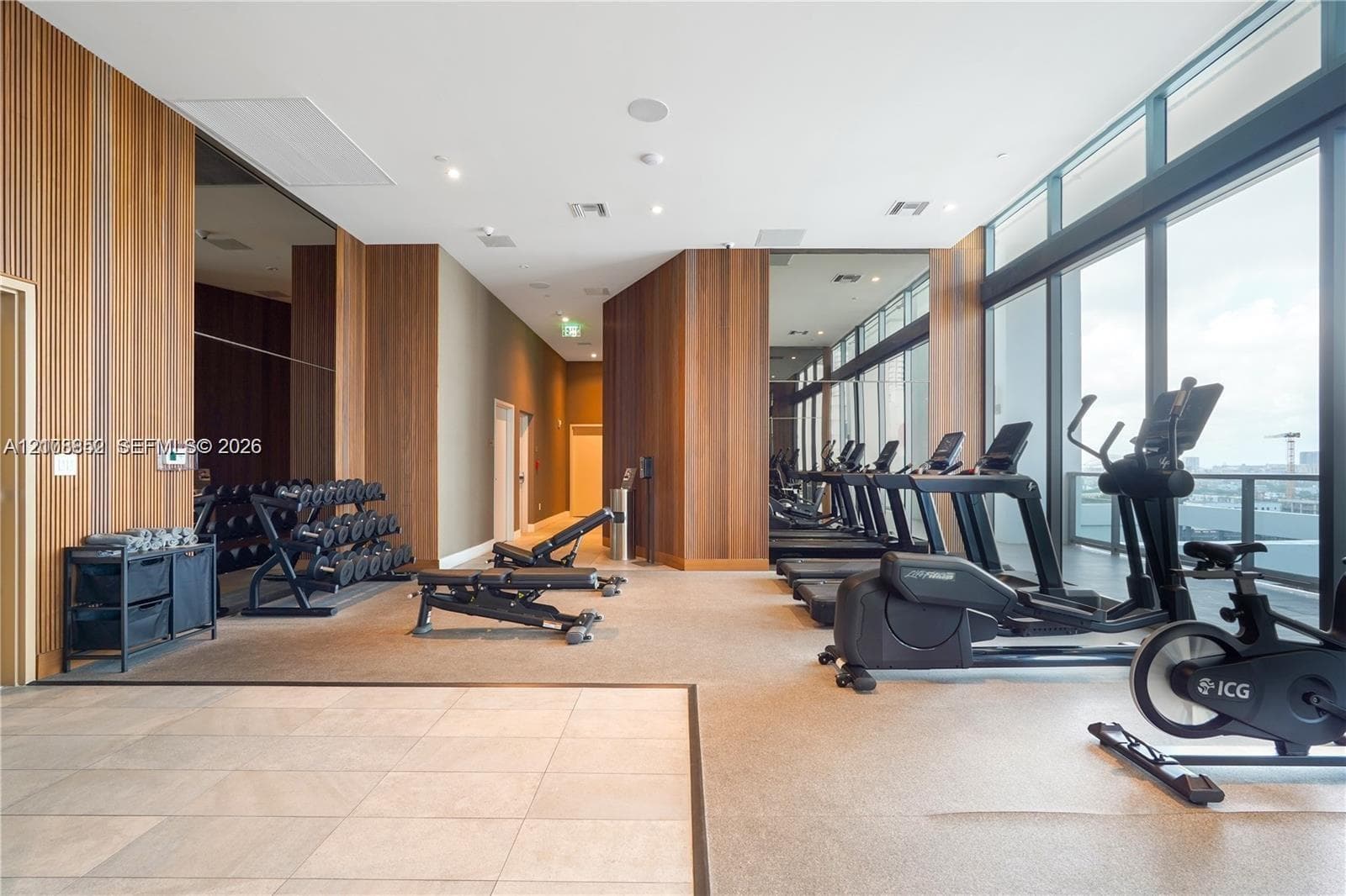 Fitness center featuring floor-to-ceiling windows, wood-paneled walls, large-format tile flooring, and integrated ceiling lighting