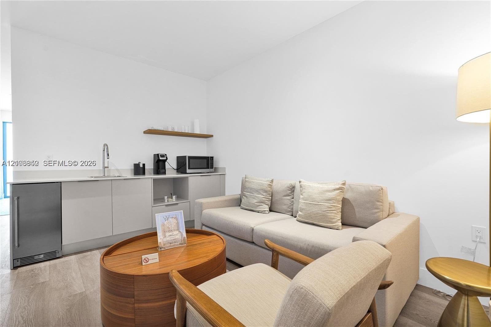Built-in kitchenette featuring light-toned cabinetry, stainless steel mini-refrigerator, inset sink with gooseneck faucet, and a floating wood-finish shelf