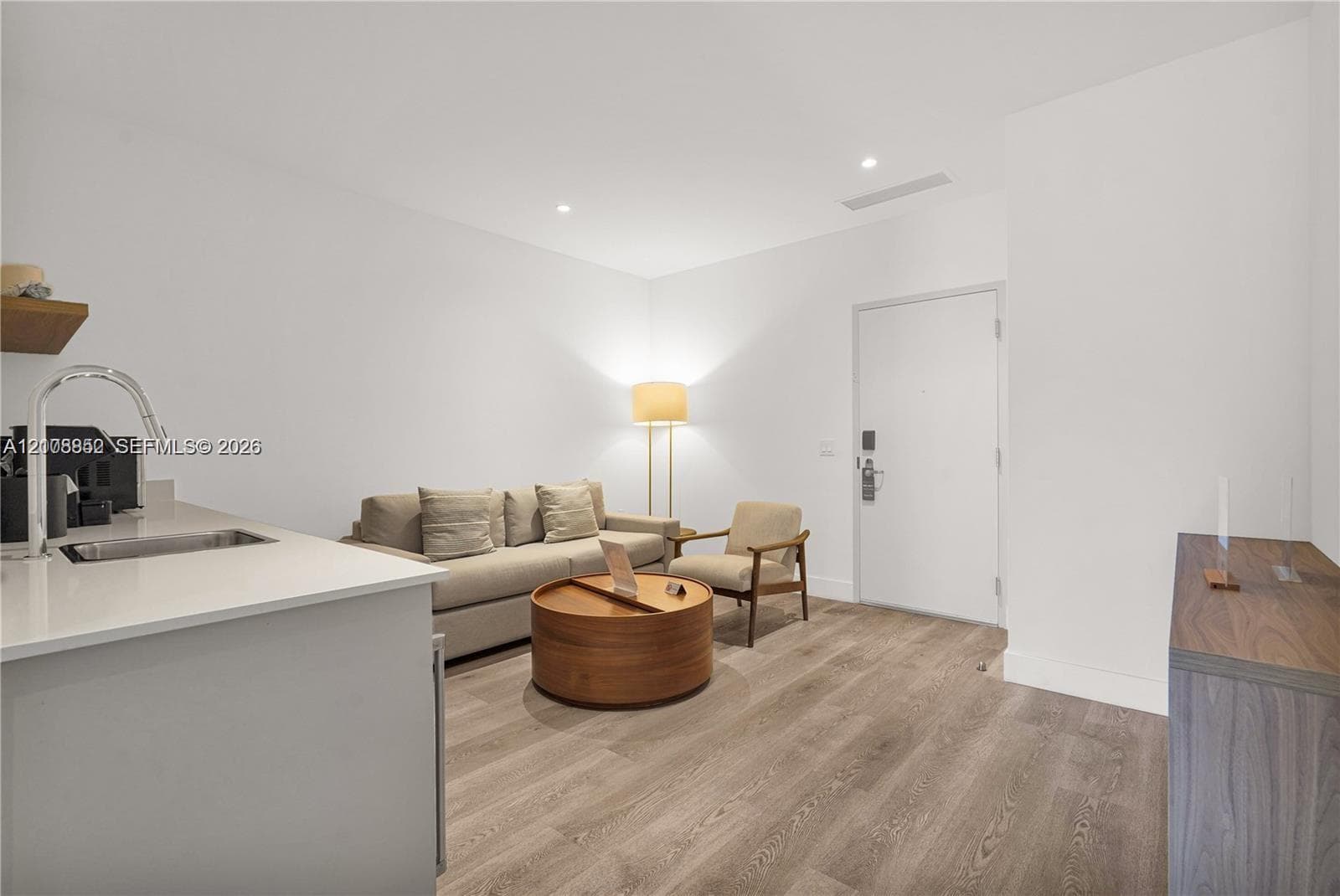Kitchenette featuring a light-toned solid surface countertop, stainless steel sink, and gooseneck faucet, complemented by wood-finish flooring and recessed ceiling lighting