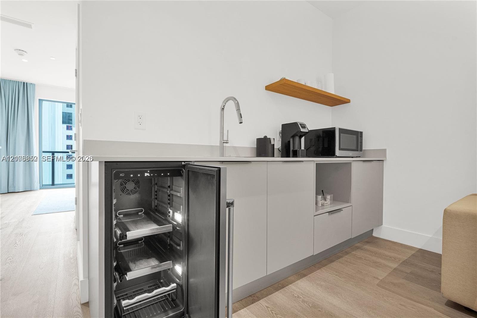 Wet bar area featuring flat-panel cabinetry, a stainless steel wine refrigerator, a stone countertop, a single-handle gooseneck faucet, and a floating wood-finish shelf