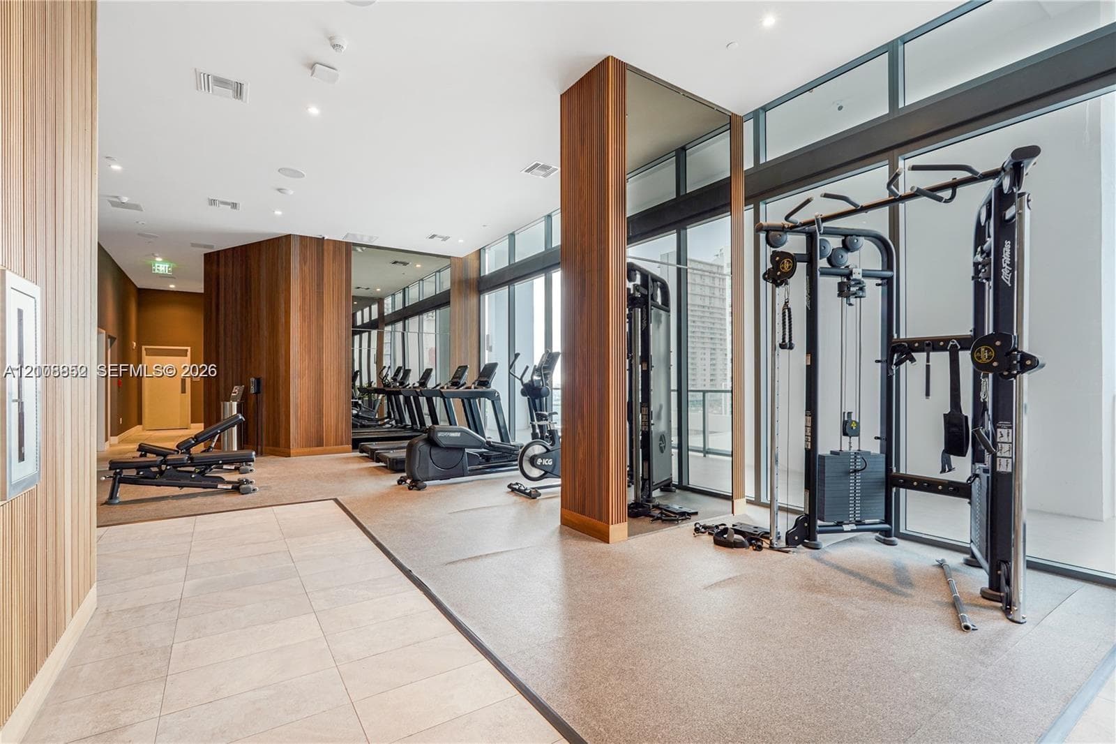 Fitness center featuring floor-to-ceiling glass windows, wood-finish wall paneling, full-height wall mirrors, and recessed lighting