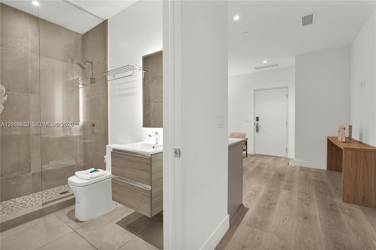 Bathroom featuring large-format tile shower walls, a glass shower enclosure with a pebble-style floor, and a wall-mounted wood-finish floating vanity