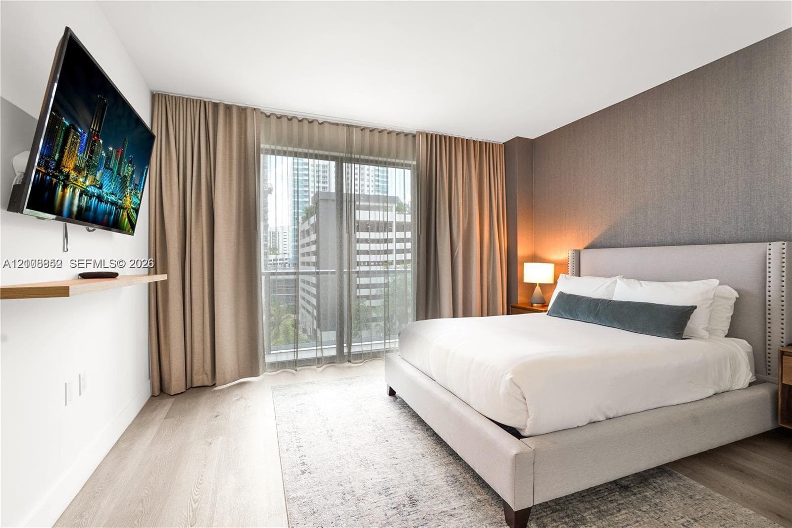 Floor-to-ceiling drapery, wood-finish flooring, textured accent wall, and sliding glass door leading to a balcony