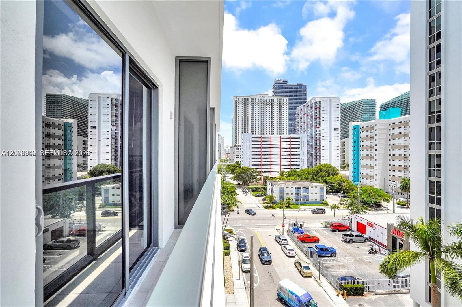 Private balcony featuring a glass-panel railing, floor-to-ceiling sliding glass doors, and expansive urban scenery
