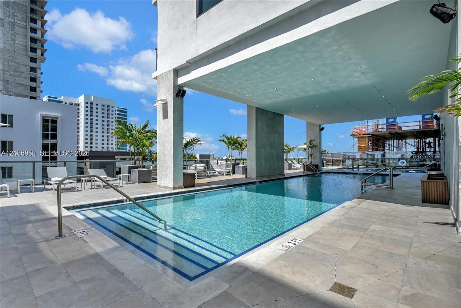 Covered terrace featuring a swimming pool with submerged entry steps, metal handrails, and large-format stone tile flooring