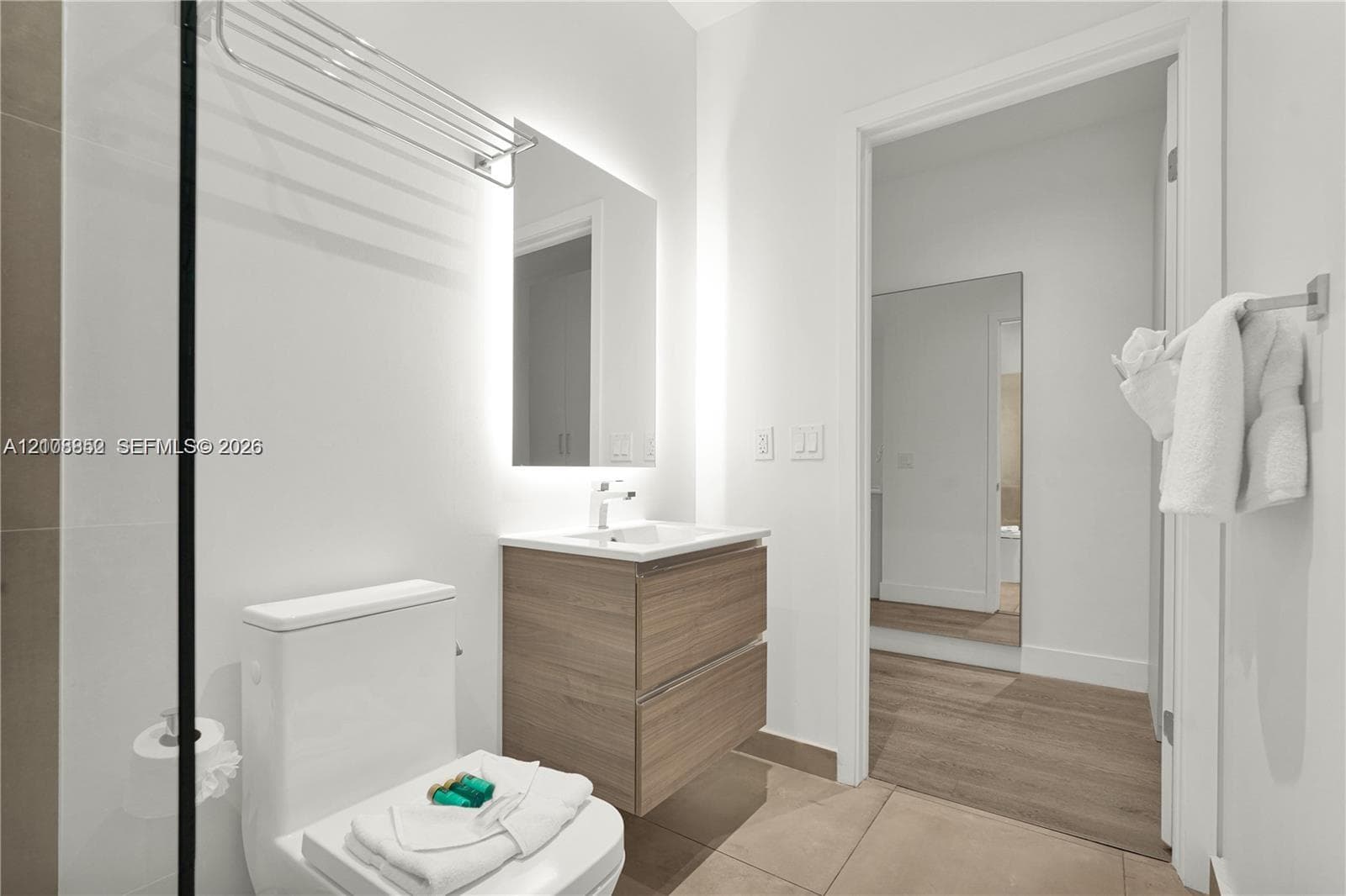 Floating wood-finish vanity with a rectangular sink, wall-mounted faucet, integrated backlit mirror, and floor-to-ceiling tilework