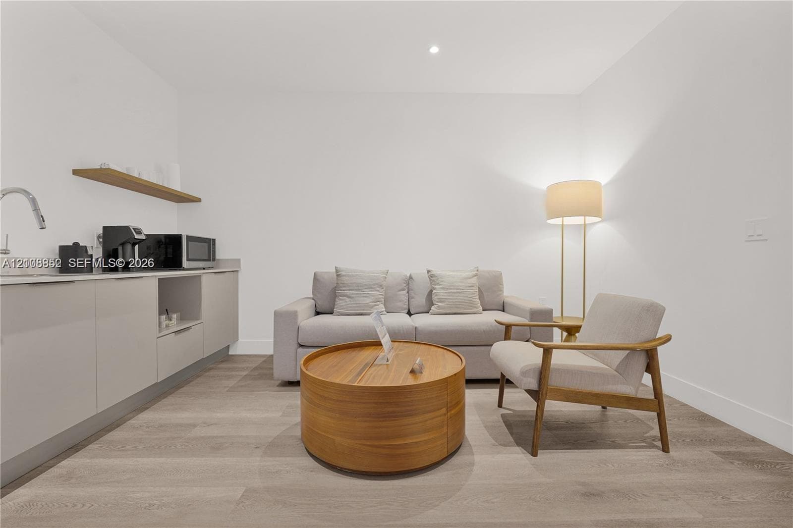 Minimalist cabinetry featuring flat-panel doors, neutral solid-surface countertops, a stainless steel faucet, and a wall-mounted floating shelf, complemented by wood-finish flooring