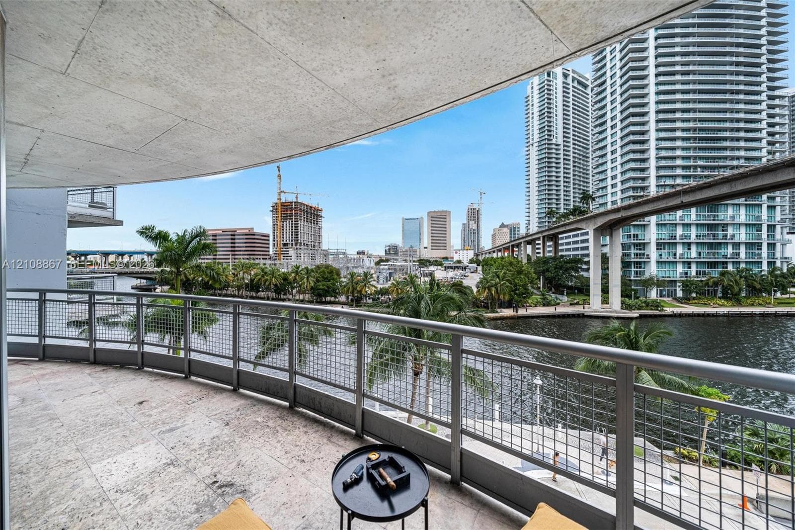 Curved balcony featuring stone flooring and metal railings, overlooking the waterfront and urban skyline